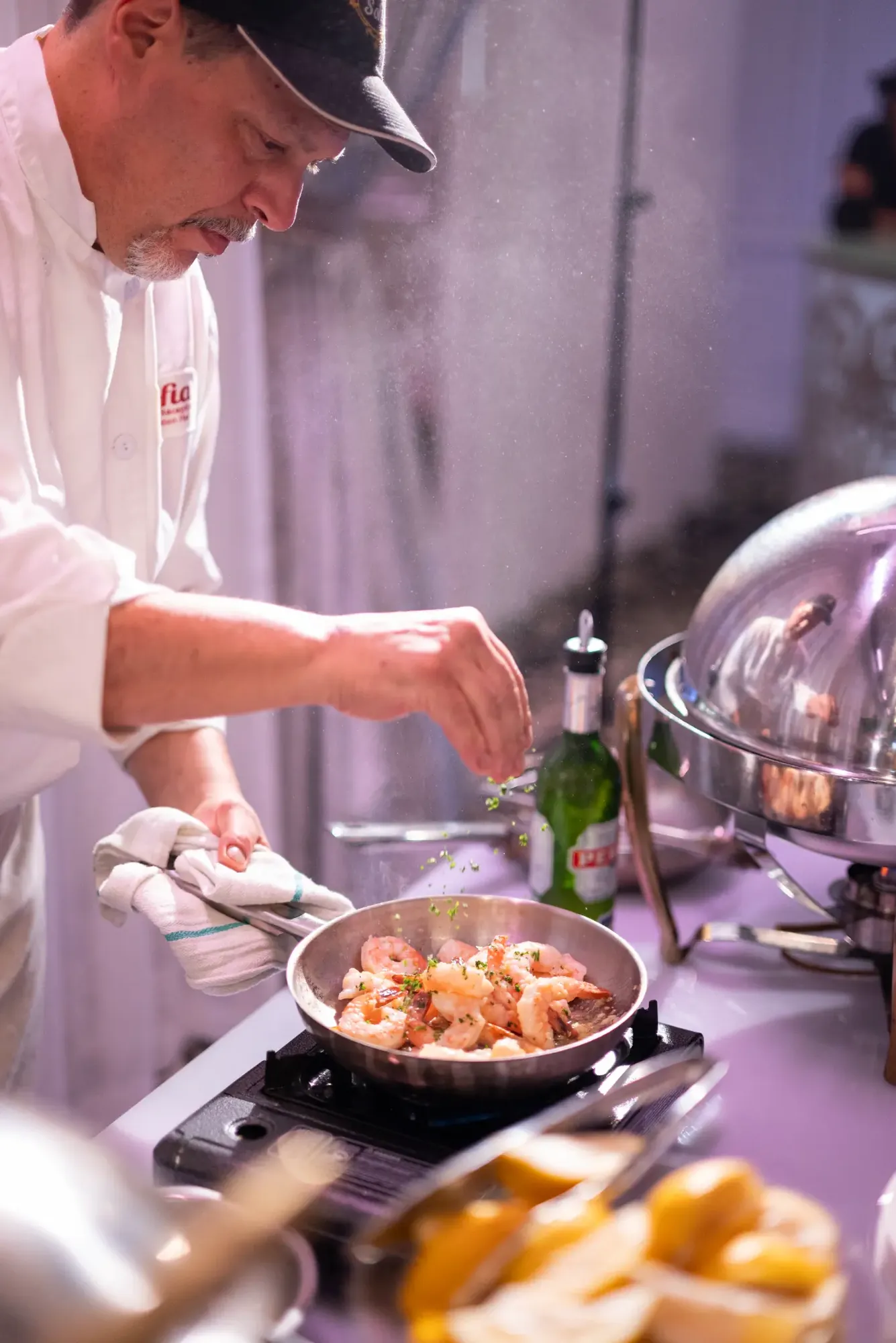 Chef saupoudrant des herbes sur des crevettes cuisant dans une poêle.