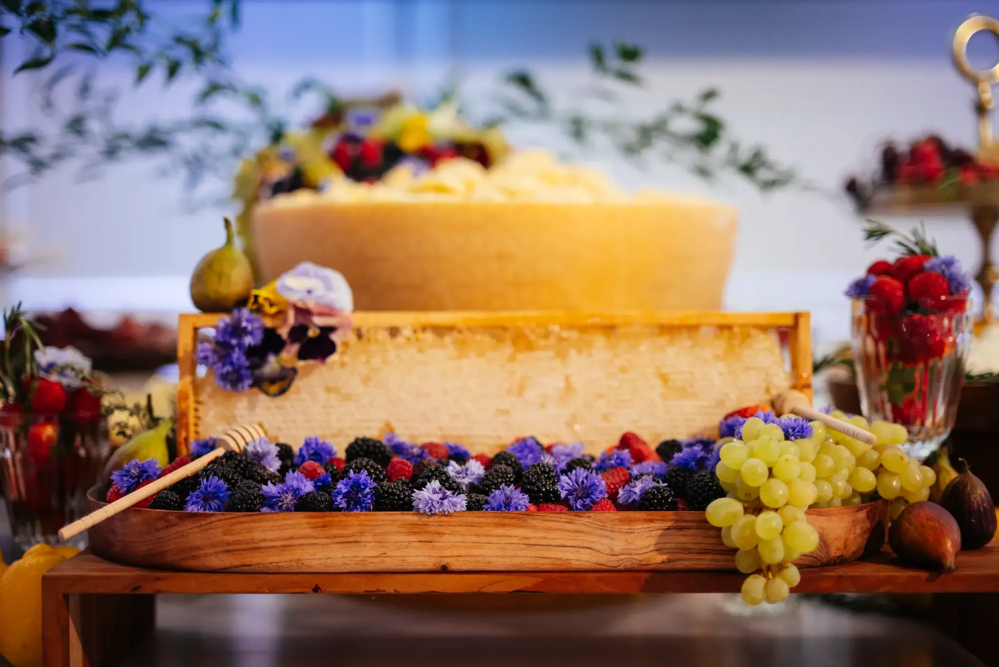 Plateau en bois avec fruits frais, rayon de miel et fleurs comestibles.